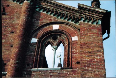 Dalla bifora sintravede la cuspide  del campanile; sotto il cornicione, archetti pensili intrecciati, sfondo bianco.